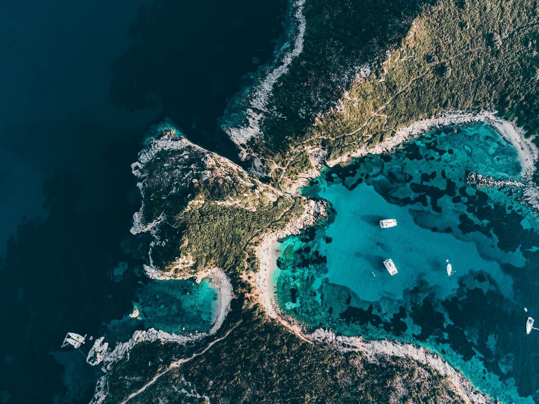 Stunning aerial view of coastline with clear turquoise waters and yachts.
